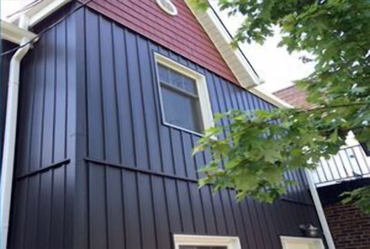 Dark board-and-batten siding with window capping and a white downspout