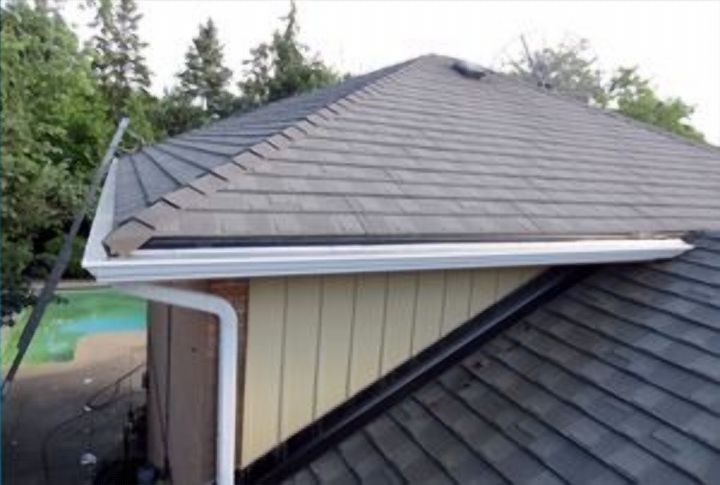Close view of a new white eavestrough and downspout at a shingled roof edge