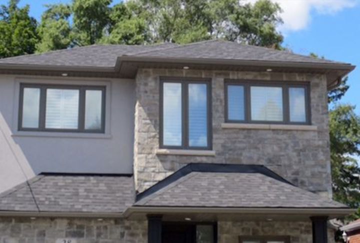 Front of a two-storey stone and stucco house with new eavestrough and dark window capping