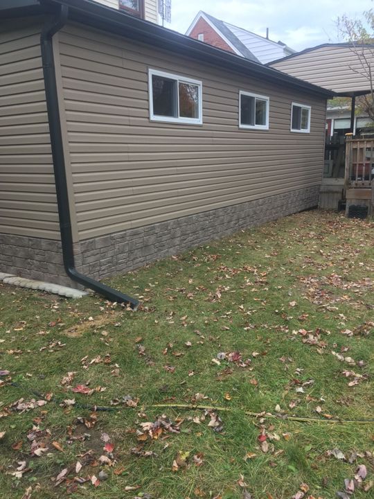 Rear addition with new beige horizontal siding, window capping and a dark downspout