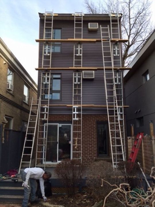 Three-storey house with ladders and scaffold planks, siding being installed