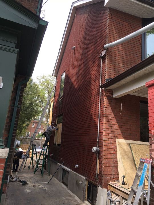 Brick side wall with new white soffit, crew member on a ladder