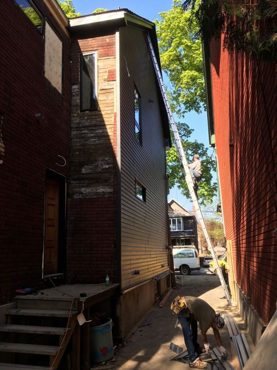 Side of a house with new dark siding going up over the old wall