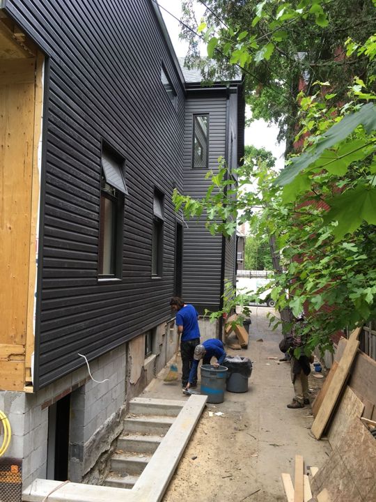 Charcoal horizontal siding and window capping on a narrow side wall, crew working below
